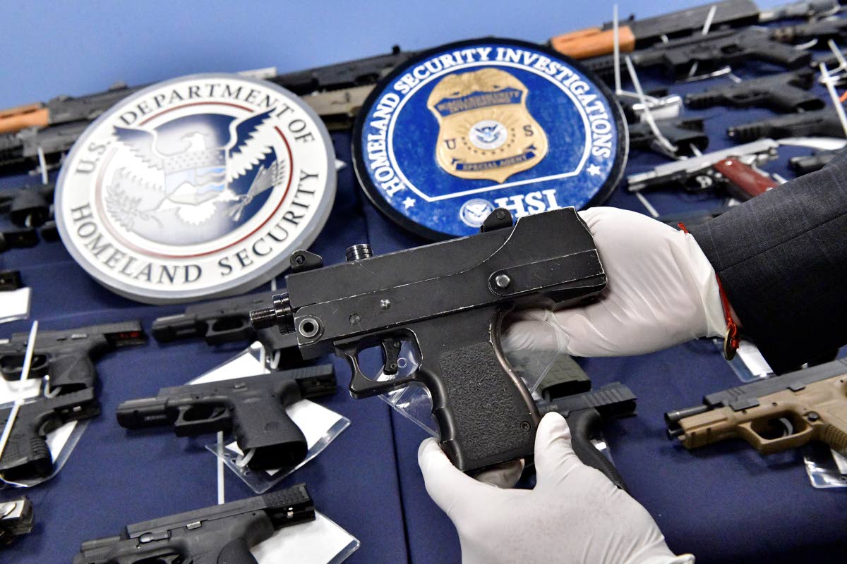An agent of Homeland Security Investigations (HSI) handles one of more than 100 firearms seized in Miami in 2017, stopping the high-powered firearms and various others from reaching its planned destination of Kingston, Jamaica.