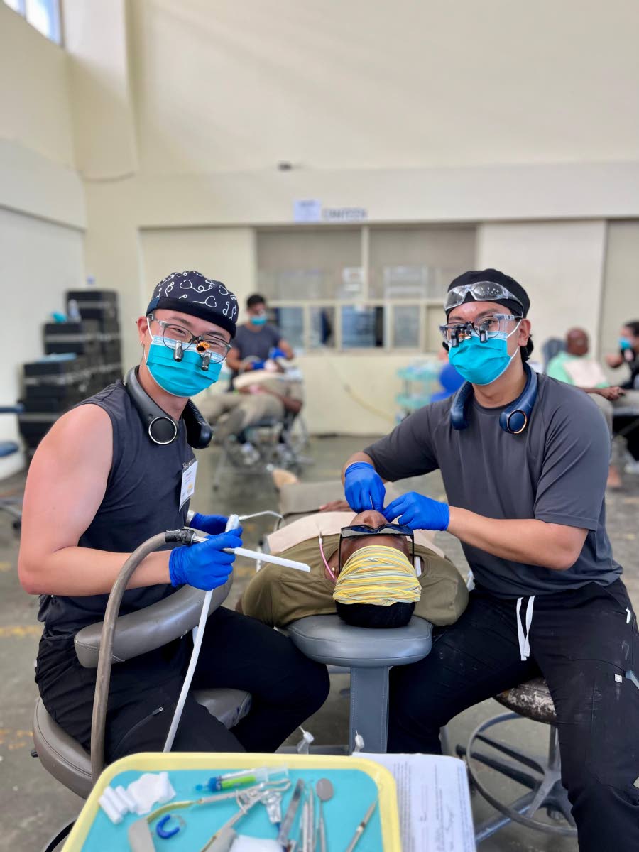 Dental practitioners Andrew Lim (left) and Ryan Elido flash masked smiles for the camera as they clean a patient’s teeth during the Great Shape! Inc. 1000 Smiles Dental Mission, held recently at William Knibb Memorial High School in Trelawny.