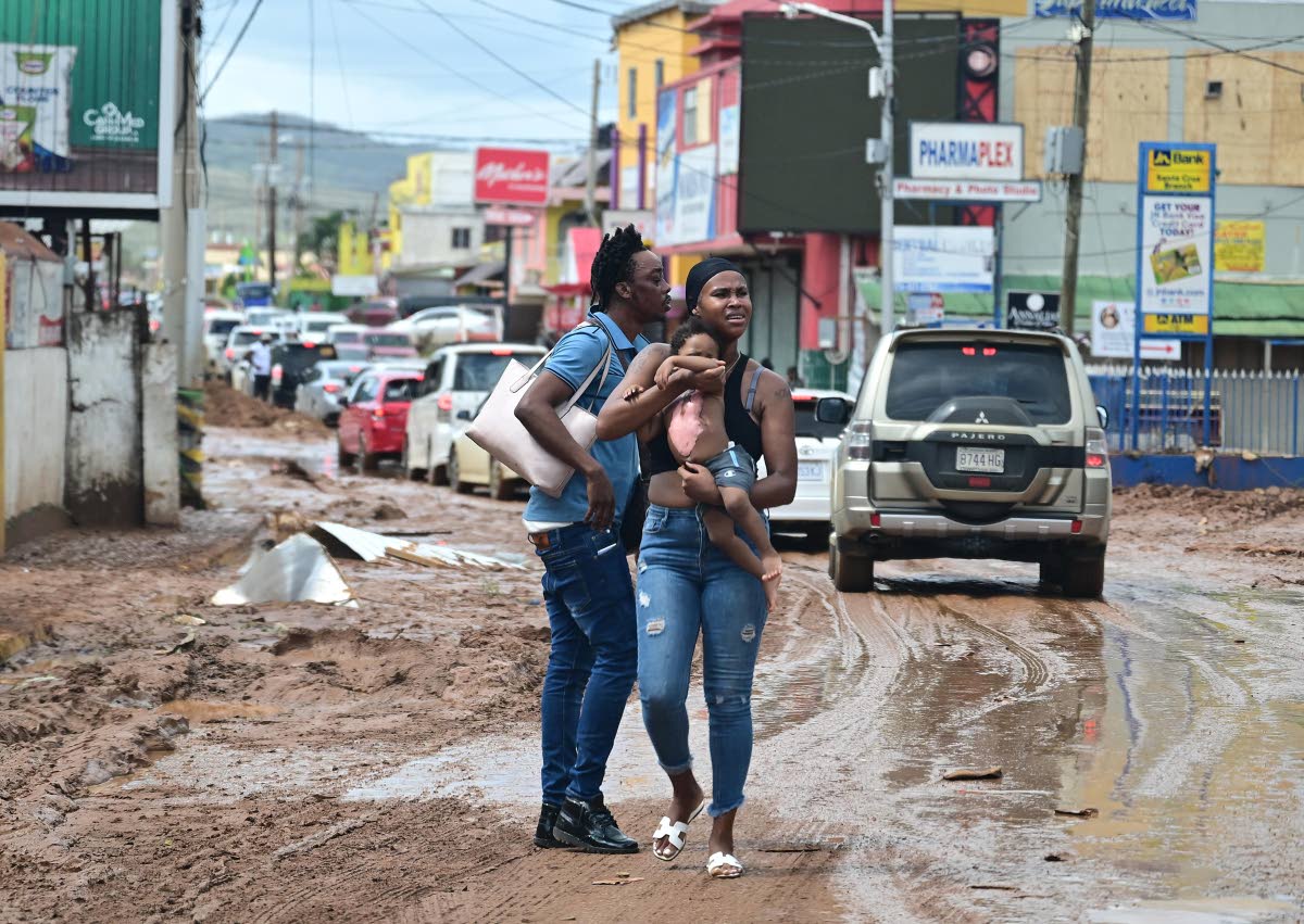 A woman holds a baby with a large burn wound on his torso in Santa Cruz, St Elizabeth, on Wednesday. She and the man accompanying her were trying to find a way to the nearest hospital. Onlookers directed them back to Mandeville, Manchester, as there was no