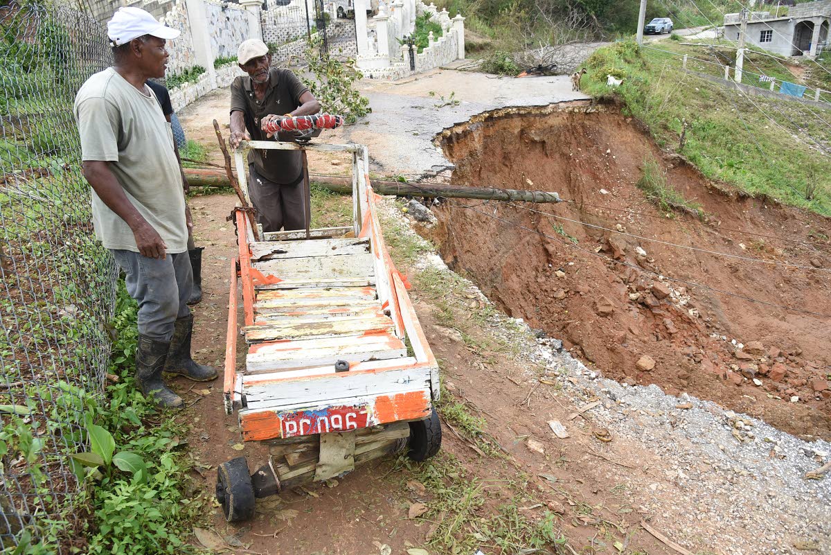 A man pushes a cart across a slither of roadway left in a section of Lorrimers, Trelawny, after a major breakway was triggered by Hurricane Melissa.