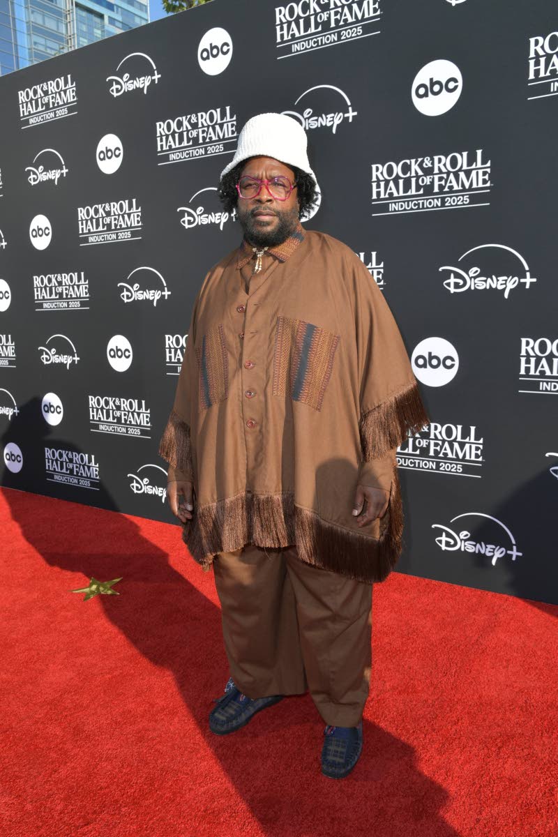 Questlove is wearing a relaxed brown fringed ensemble featuring an oversized shirt jacket with woven detailing and fringe trim along the sleeves and hem, paired with matching loose trousers. He completed the look with dark slip-on shoes, a white bucket hat
