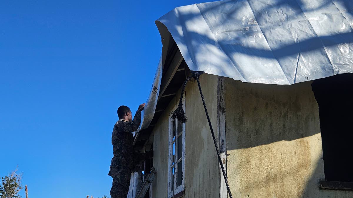 A member of the JDF assists with the laying of a tarpaulin on a roof in Granville, Trelawny last week