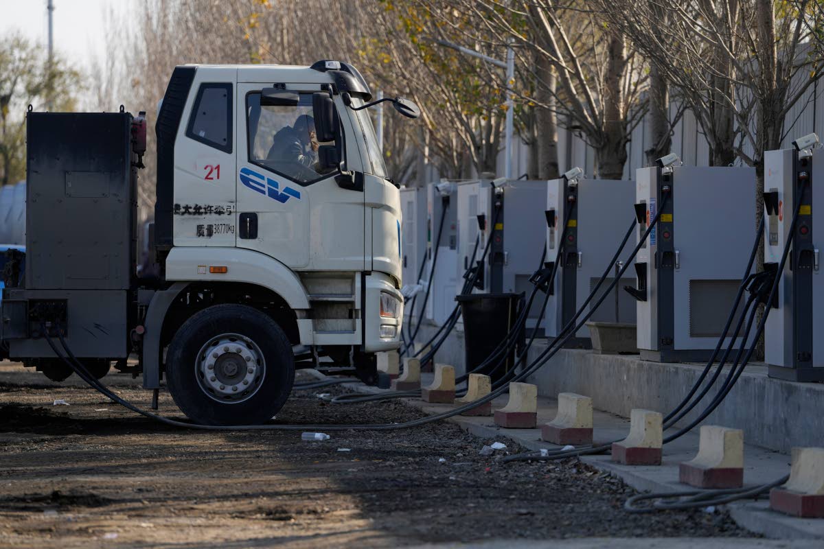 A driver rests in the cabin as his electric truck is plugged into a charging station on the outskirts of Beijing, on November 14, 2025.