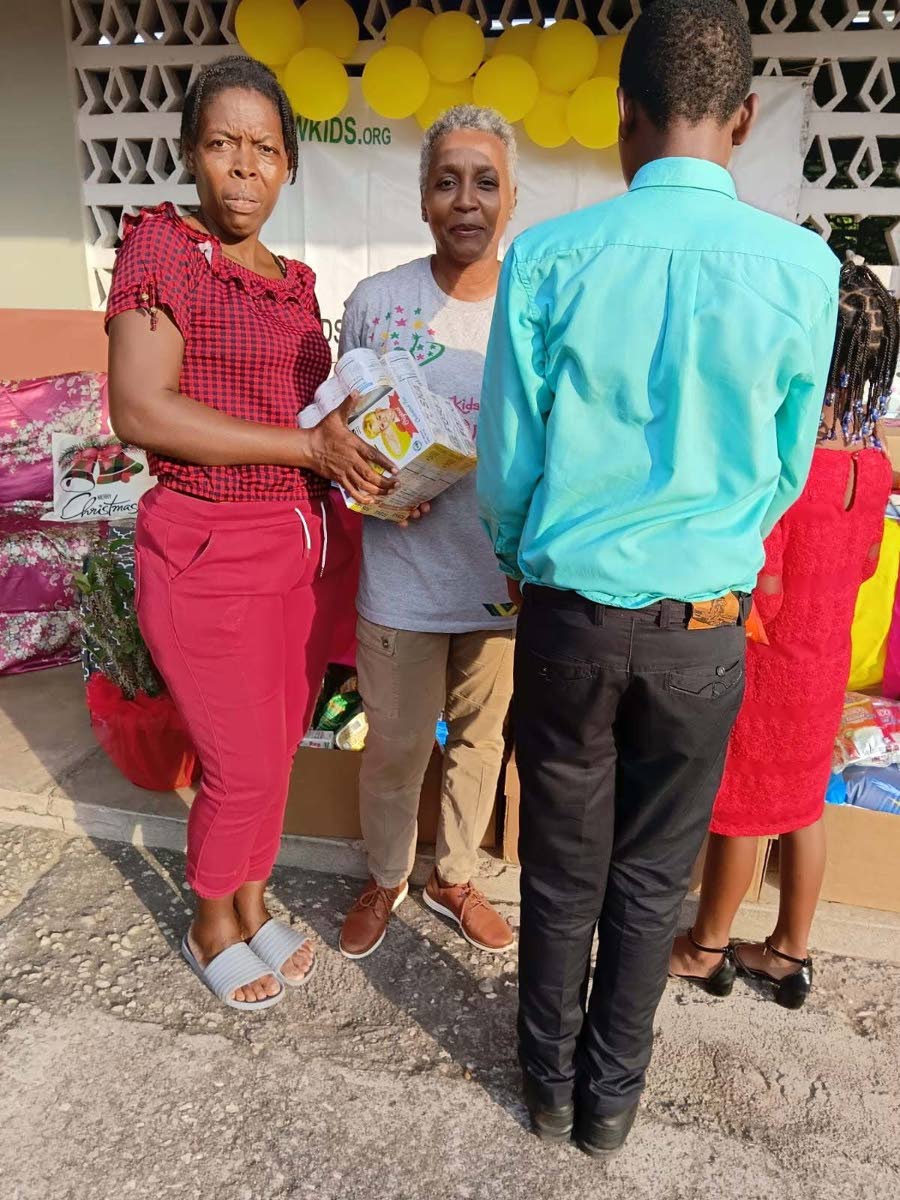 Simone Sobers (centre), founder and president of Winsome Wishes for KIDS, presents grocery items to a parent during a Christmas treat at Morgan’s Pass Primary in Clarendon. At right are the parent’s children, whose faces have been concealed.
