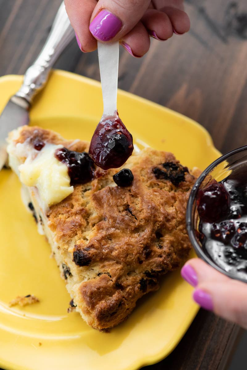 A slice of dried cherry scone is topped with grape jam.