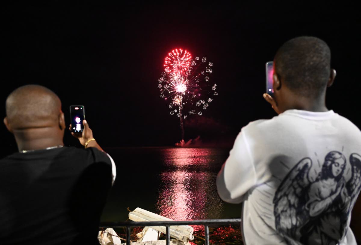 Two men photograph fireworks over Black River’s seafront.