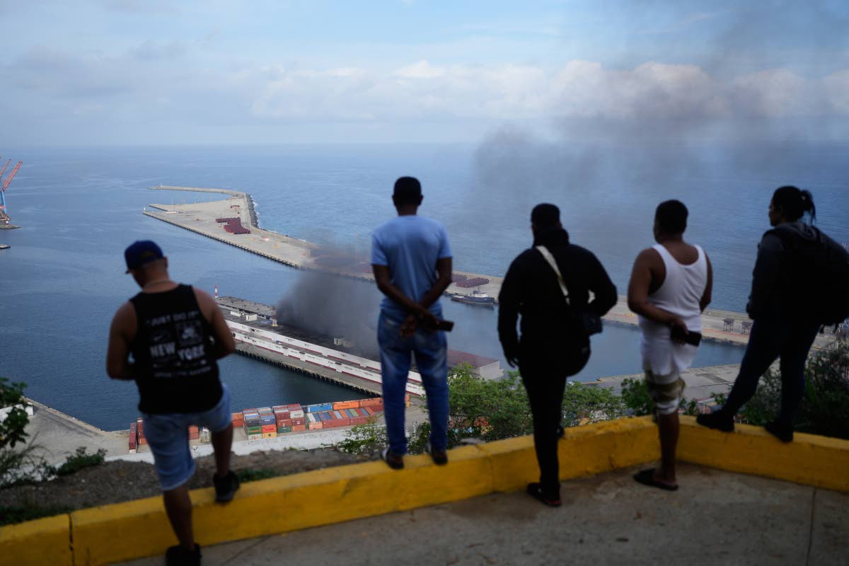 Men watch smoke rising from a dock after explosions were heard at La Guaira port, Venezuela, on Saturday.
