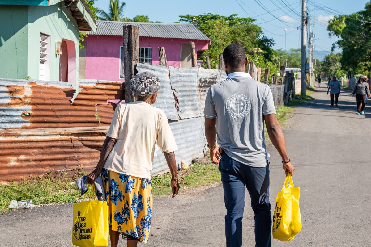 Jevauhn Robinson (right), junior systems & database administrator, Jamaica Broilers Group, walks alongside McCook’s Pen resident Maude Henry (left), as she guides him to deliver care packages to her neighbours during the company’s community outreach.