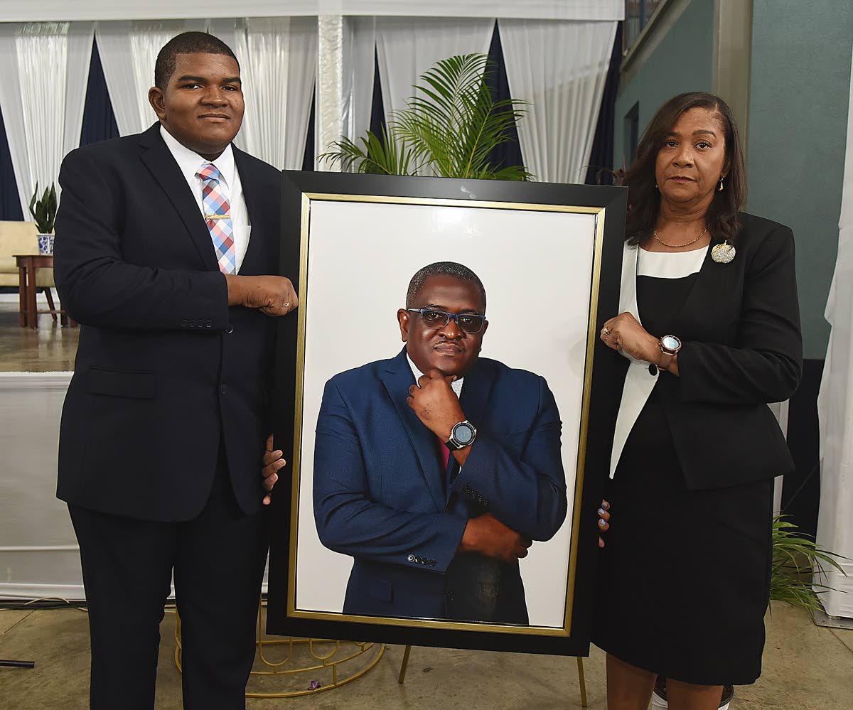 Daniel Smith, son of Anthony Smith, and his mother, Karen Smith, hold a photograph of Anthony Smith, former CEO of the RJRGLEANER Communications Group, during a thanksgiving service for his life held yesterday inside the Karl Hendrickson Auditorium at Jama