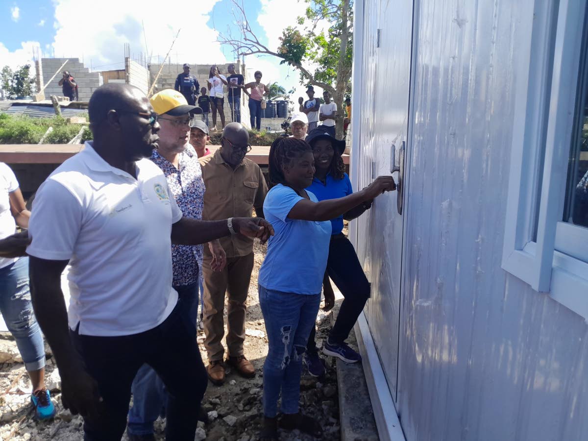 Theresa Weddeburn joyfully turns the key to open her new home, while enjoying the moment with her are (from left) Hilroy McFarlane, managing director of C M Recycling (the donor agency of the container House); Opposition Leader Mark Golding; Mayor of Lucea