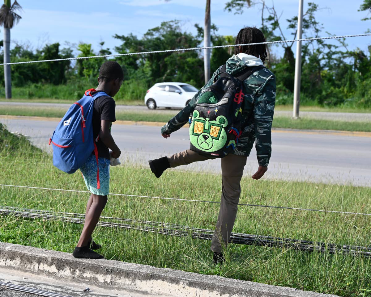 
Two young children carefully cross downed cable wires on their way home from school in Rose Hall, St James, last Friday.