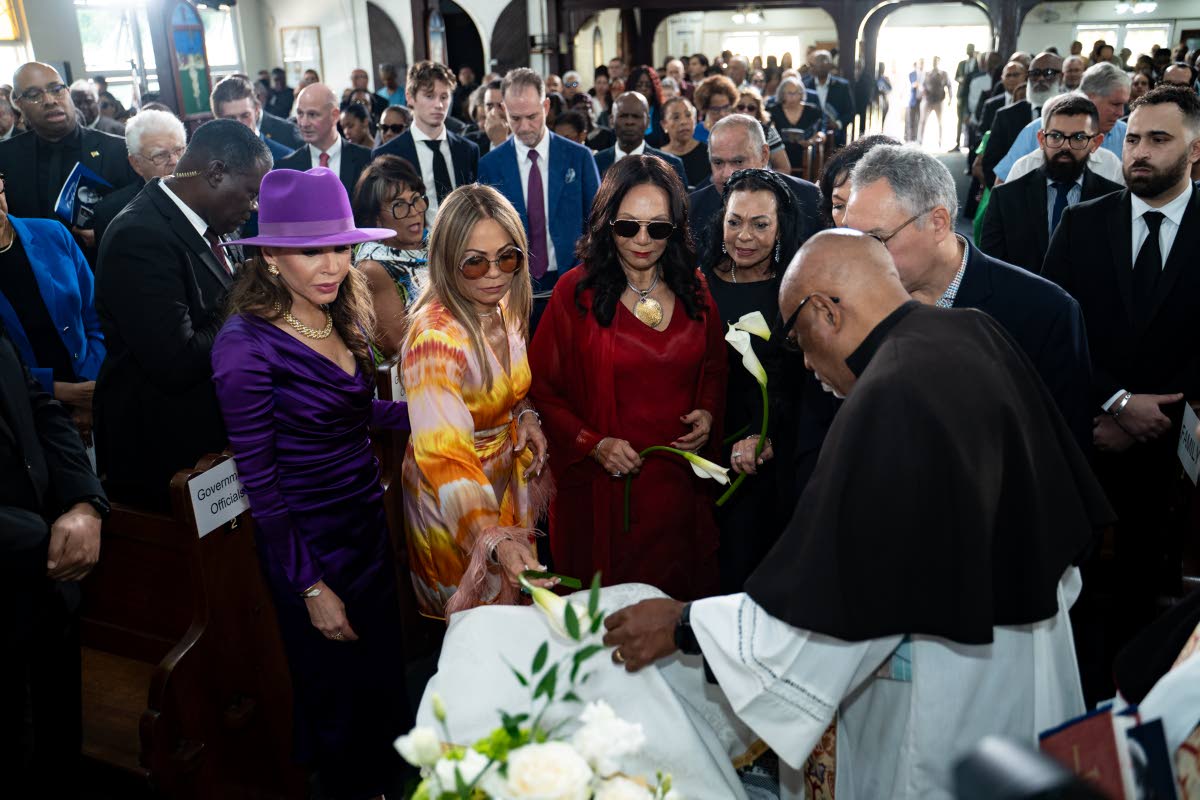 Michelle Bovell (centre in red), widow of Christopher Bovell, and her daughters place a lily by her husband's urn.