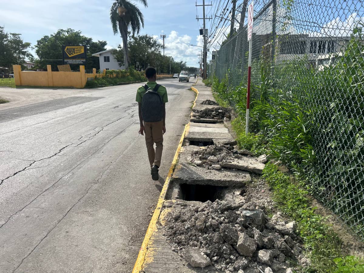 The crumbling sidewalk in front of the National Works Agency office along Barracks Road in Savanna-la-Mar, Westmoreland, forces this student to walk on the road surface.