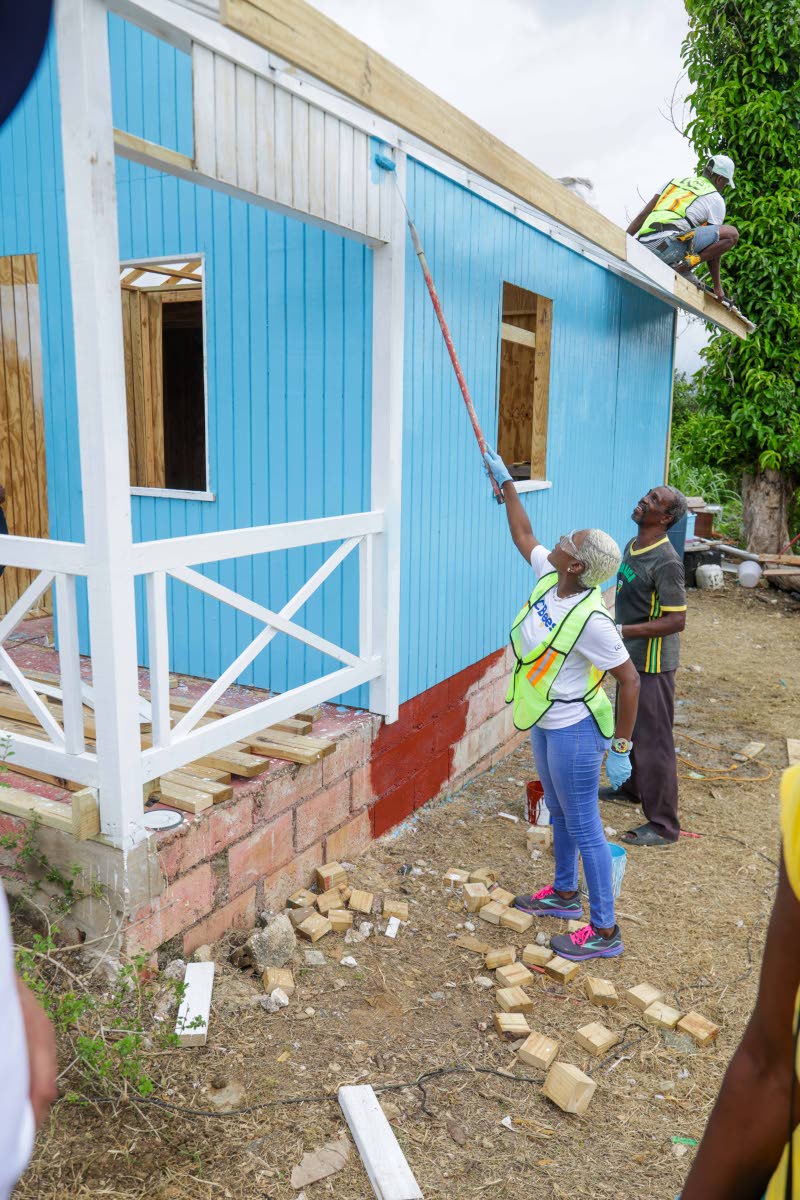 Sharon Williams, director, NCB Foundation, applies a final coat of paint as Hubert Samuels prepares to welcome his family back into their restored Black River home. 