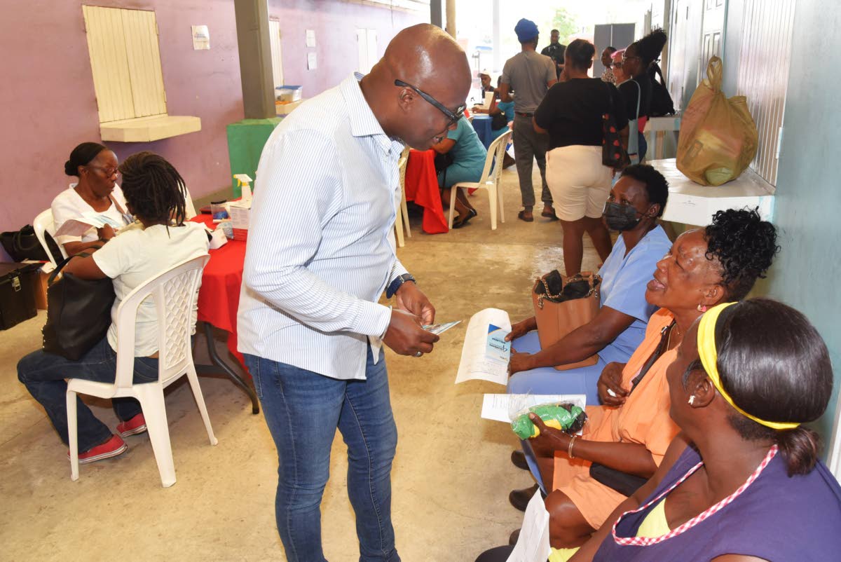 City Inspector for the Kingston and St Andrew Municipal Corporation (KSAMC), Alrick Francis (left), greets visitor to the KSAMC Health Expo, Hope Uter (seated, centre). 
