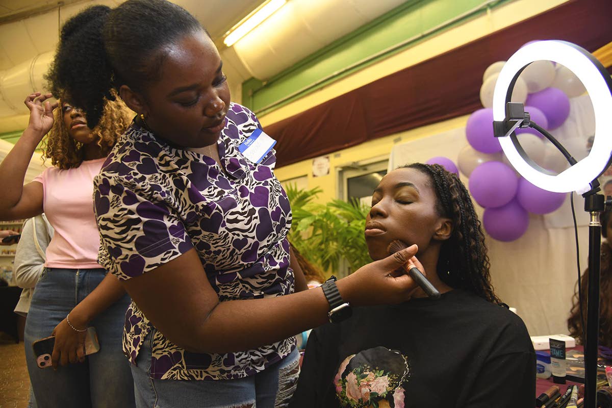 Simone Rowe, make-up artist at Sim Touches, does the make-up of Tianna Scarlett, first year international relations student, at Rex Nettleford Hall’s business expo held on Wednesday.