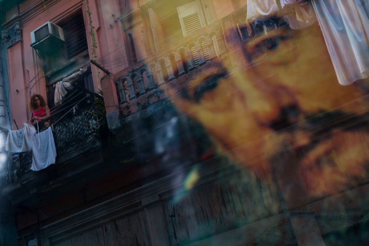 A Cuban woman hanging laundry on her balcony is seen reflected in a glass window decorated with a poster of Cuba's leader Fidel Castro in Old Havana, Cuba on December 27, 2007. (AP Photo/Dado Galdieri, File)