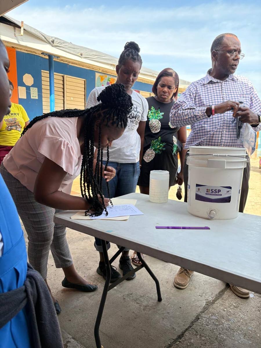 Eager parents line up to receive their water filters during the distribution at Broughton Primary School while a prototype filter sits on display on a table.