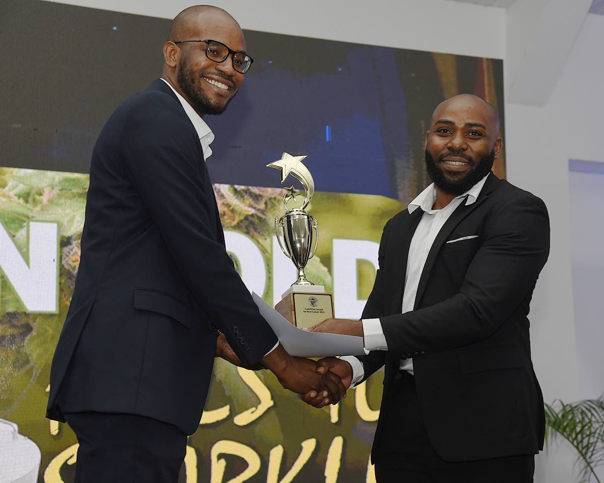 The Gleaner’s Jovan Johnson (left), who won five individual awards at the National Journalism Awards ceremony, collects one of them from Charles Barrett, general manager of operations at Caribbean Dreams Food Limited.