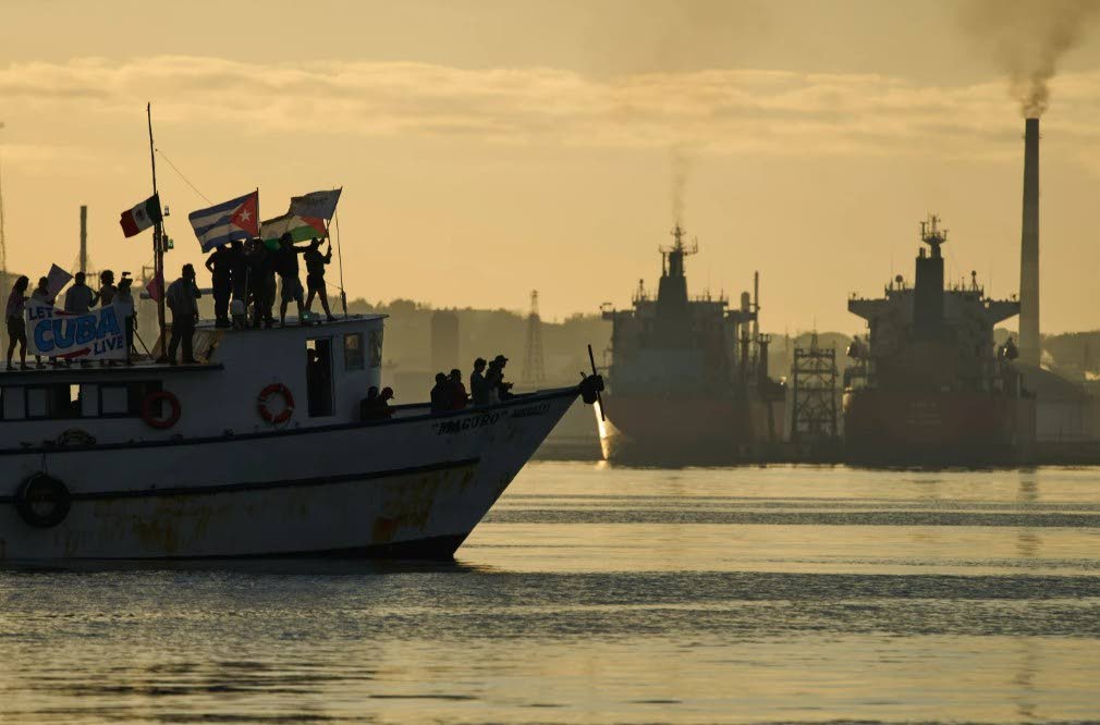 Activists wave Cuban and Palestinian flags from the vessel Maguro, arriving from Mexico with humanitarian aid as part of the "Nuestra America," or Our America convoy, in Havana Bay, Cuba, Tuesday, March 24, 2026. 