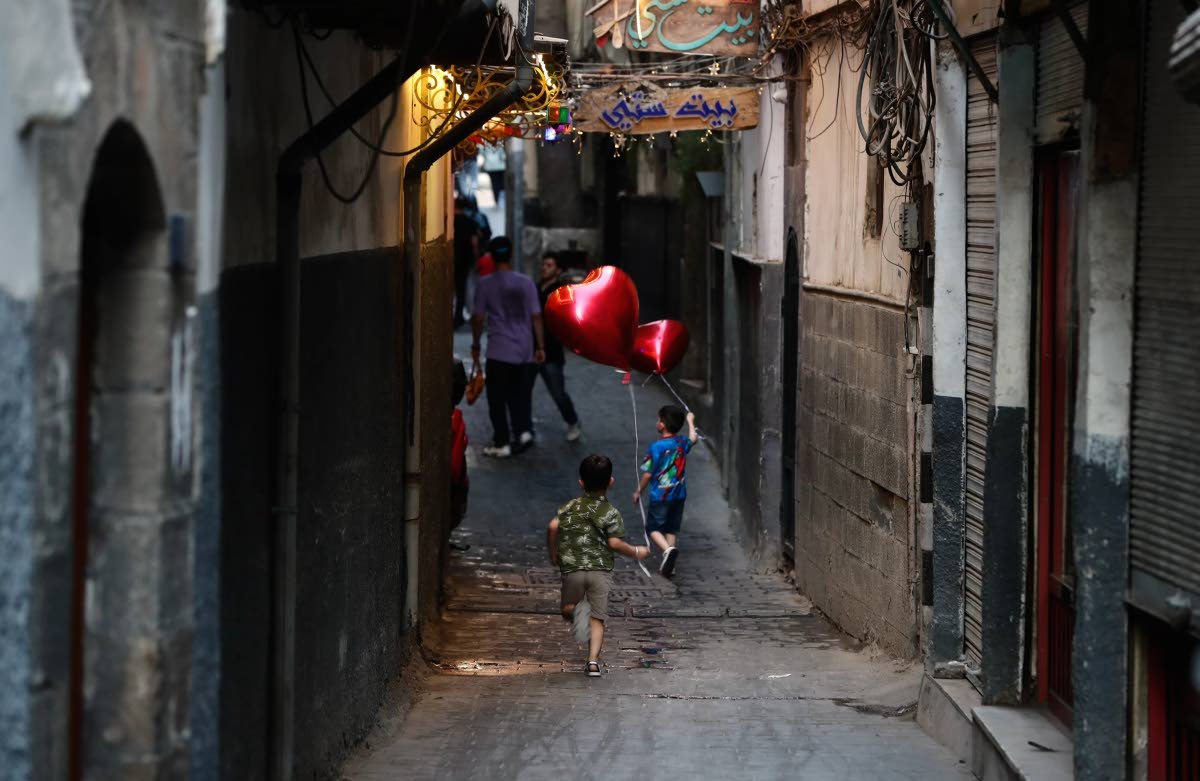 Children holding heart-shaped balloons on a string head down an alley in the Old City of Damascus, Syria, Thursday, July 23, 2026. 