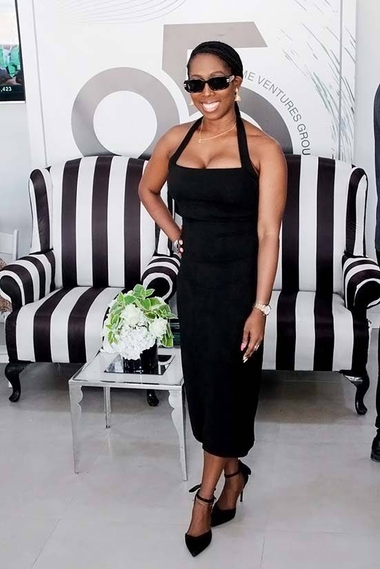 Dominique Martin wears a sleek form-fitting black halter dress, pairing it with square sunglasses and black pointed-toe stiletto pumps with delicate ankle straps.