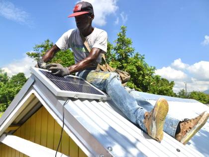 Demar Banton a carpenter working with Food For The Poor installs a solar panel on the roof of a newly bult house for a family in Kingston.