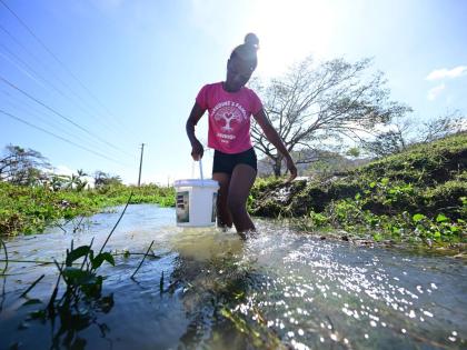 A young woman fills a bucket with water to wash clothes at the Blue Hole along the Sandy Bay main road in Hanover last month as there was no water supply in her community.