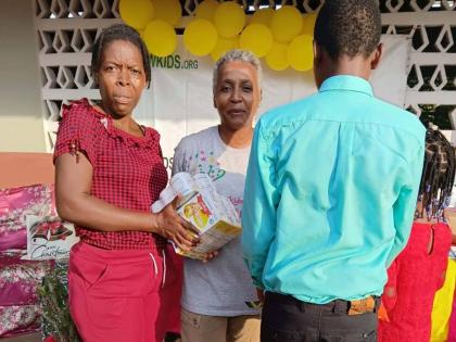 Simone Sobers (centre), founder and president of Winsome Wishes for KIDS, presents grocery items to a parent during a Christmas treat at Morgan’s Pass Primary in Clarendon. At right are the parent’s children, whose faces have been concealed.
