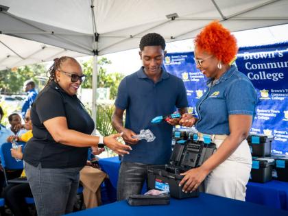 JPS Foundation Head Sophia Lewis (right) and Brown’s Town Community College Claudeth Haughton look on as Electrical Installation Level II student Rajaunie White unpacks items in his electrical toolkit donated by the foundation.