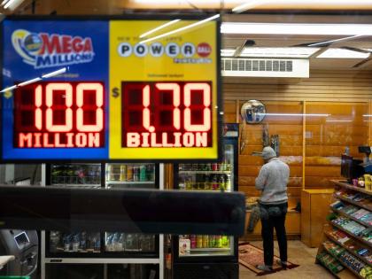 A convenience store employee prays while Jackpot payouts for Powerball and Mega Millions are displayed outside the store, Tuesday, December 23, 2025, in New York. (AP Photo/Yuki Iwamura)
