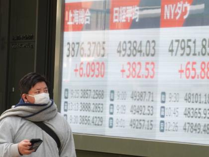 
A person walks in front of an electronic stock board showing the market indexes of Shanghai, Tokyo and New York Dow at a securities firm in Tokyo, Japan. 