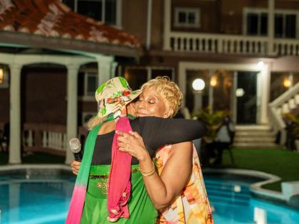 Dr Marcia Griffiths (left) shares a warm embrace with fellow reggae songstress Nadine Sutherland during the postgraduation reception at her home, moments after Sutherland delivered a moving tribute in honour of the newly conferred cultural icon.