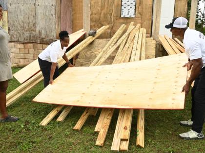 From left: Tanekia Titus looks on as Hermine Pryce Foundation co‑founders Andrea Pryce and O’Neil Pryce lift a sheet of plywood donated to her at her home in Bunkers Hill, Trelawny.
