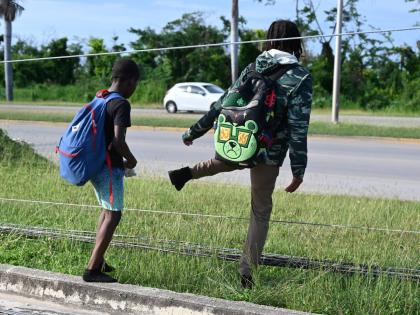 
Two young children carefully cross downed cable wires on their way home from school in Rose Hall, St James, last Friday.