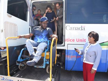 Leco Bradford smiles as Marisa Dalrymple‑Philibert (right), minister of state in the Ministry of Justice and Constitutional Affairs, operates the lift to assist him on to the Justice Bus. Looking on are Dian Watson (left), executive director of the Legal