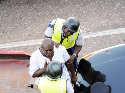 A man stands between his car and a wrecker to avoid the towing of his car in downtown Kingston in 2011. He was allegedly caught after being chased by the police and Transport Authority inspectors.