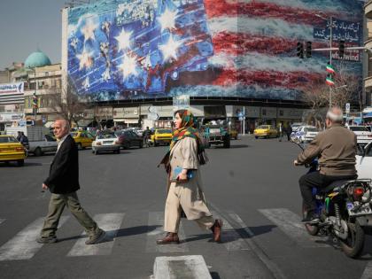 Pedestrians walk past a billboard depicting a US aircraft carrier with damaged fighter jets on its deck and a sign in Farsi and English reading, ‘If you sow the wind, you’ll reap the whirlwind,’ at Enqelab-e-Eslami (Islamic Revolution) Square in Tehr