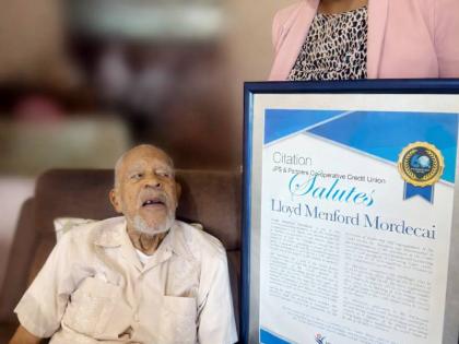 Camille Archibald, business development manager of JPS & Partners Co-op Credit Union, presents a citation to Lloyd Menford Mordecai, whose early efforts helped lay the foundation for the strong credit union we know today.