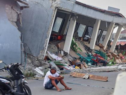 A man checks his phone near a building collapsed due to an earthquake, in Reok, East Nusa Tenggara province, Indonesia, Sunday, Aug. 16, 2026. (AP Photo/Aquila Handayani Abbas)