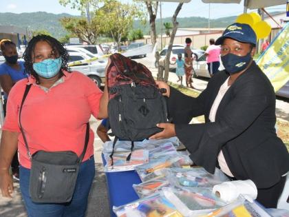 Karen Clayton (right), the regional administrator at the Western Parks and Markets (WPM) Waste Management Limited, hands over a school bag to street sweeper Tamara Chambers, during a recent book drive and back-to-school treat in Montego Bay, St James. 