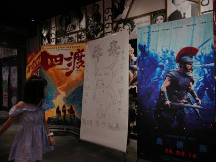 A man girl walks by a drawing poster promoting a Chinese animated film ‘Niu Lai’ on display with other movie posters at a cinema in Beijing on Tuesday.