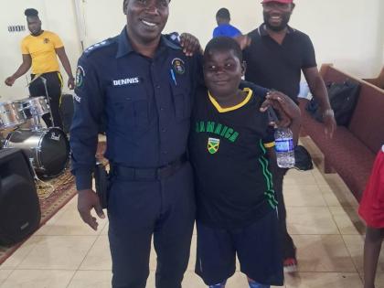 Superintendent Odaine Dennis, commanding officer for the Manchester Division, greets and poses with a young camper last week.