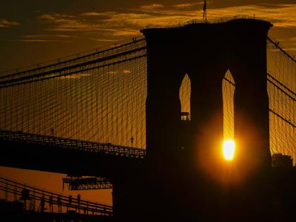 FILE - The sun rises behind the Brooklyn Bridge on Oct. 11, 2023, in New York. (AP Photo/Kiichiro Sato, File)