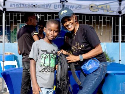 Suzanne Brown (right), administrative assistant, system operations, Jamaica Public Service, presents Ricardo Clarke with a new backpack during a community back-to-school treat at Waterhouse in Kingston on August 30.