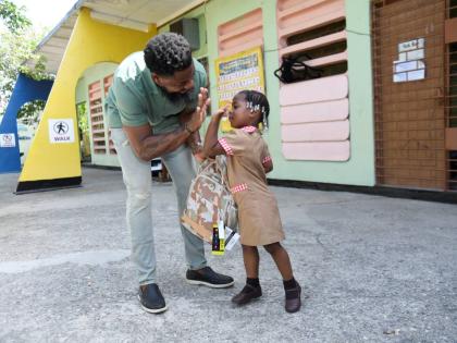 Businessman Oneil ‘Brisco’ Brissett gets a high-five from Mylah Haughton, one of six students who benefited from his back-to-school giveback at Waterford Infant School on Monday.