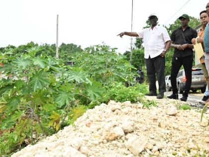Minister of Local Government and Community Development, Desmond McKenzie (left), assesses the condition of the main road in Top Burnt Ground, St Elizabeth, on Friday (October 9), where plans are being considered for the construction of a retaining wall to 