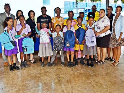 Students from Newstead Primary School in Cascade, St Mary, pose with Keron Erwin Morris (left), Cienna Smith (right), members of the Jamaica Real Estate Hub and sponsors, after receiving school bags and supplies.