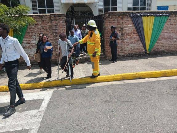 Fire personnel help a man on crutches to evacuate the courthouse following the security threat at the St Catherine Parish Court.