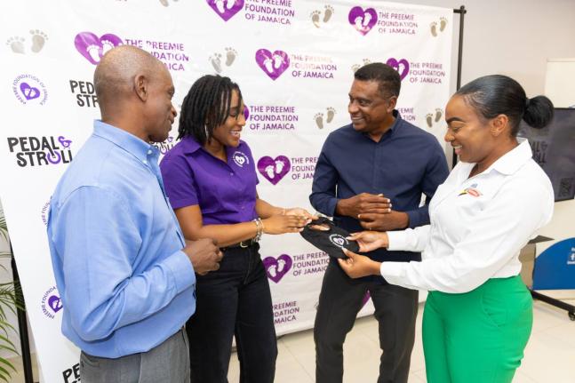 Serika Sterling (second left), founder and chairwoman, Preemie Foundation of Jamaica, shows a premature baby bib made in honour of premature babies fighting for life to (from left) Dr Wayne Palmer, president, The Jamaica Cycling Federation; Courtney Cephas